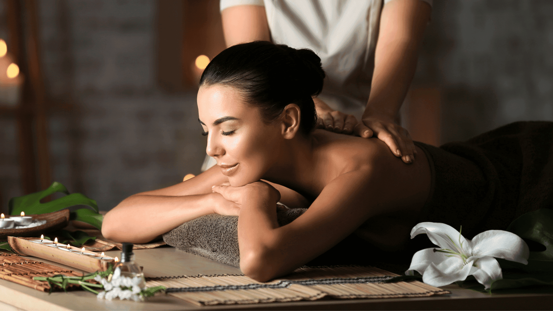 Woman enjoying a relaxing massage in a tranquil spa setting with candles and flowers.