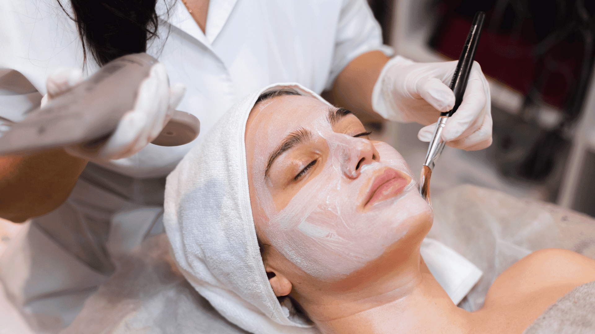 Person receiving a facial treatment with a brush and a device, relaxing under a towel.