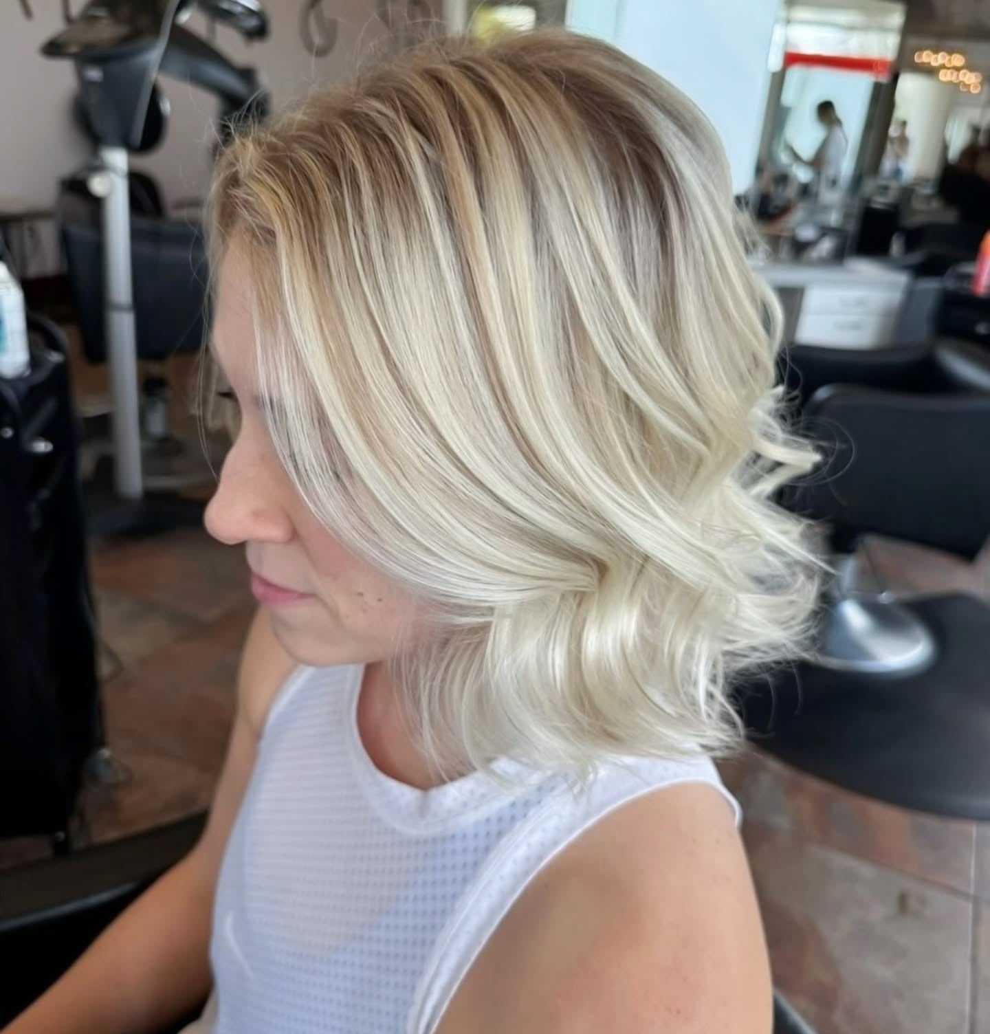 Short blonde haircut with soft waves in a salon setting.