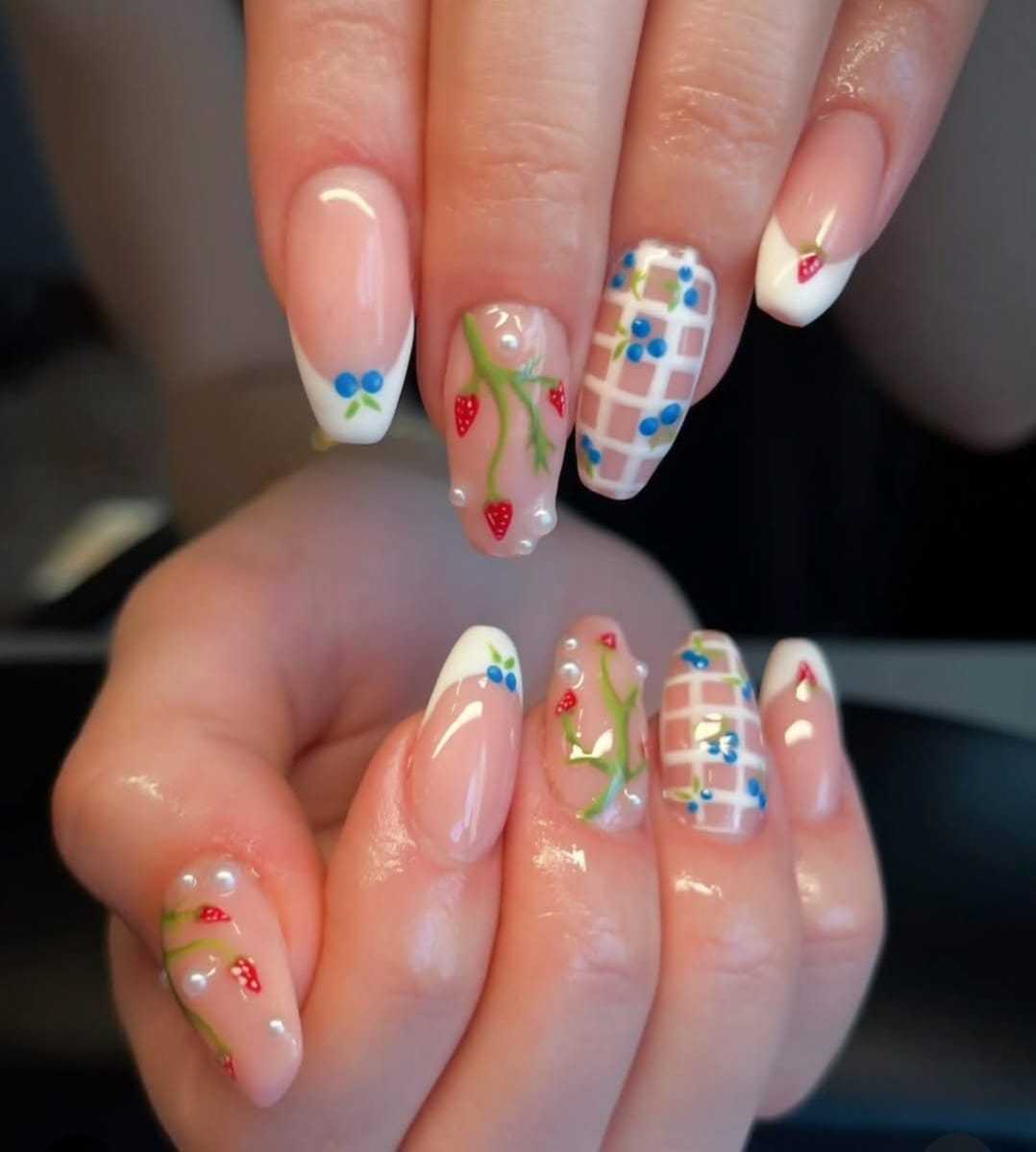 Colorful nail art with strawberries, flowers, and geometric designs on manicured nails.