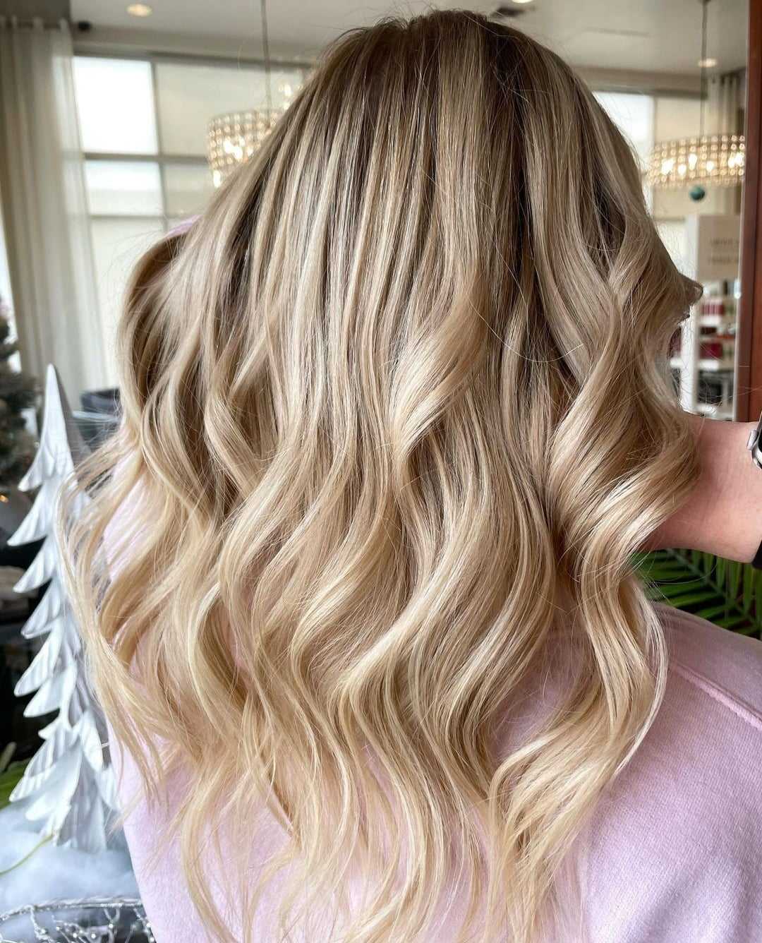 Curly blonde hair with soft highlights cascading over a pink sweater.