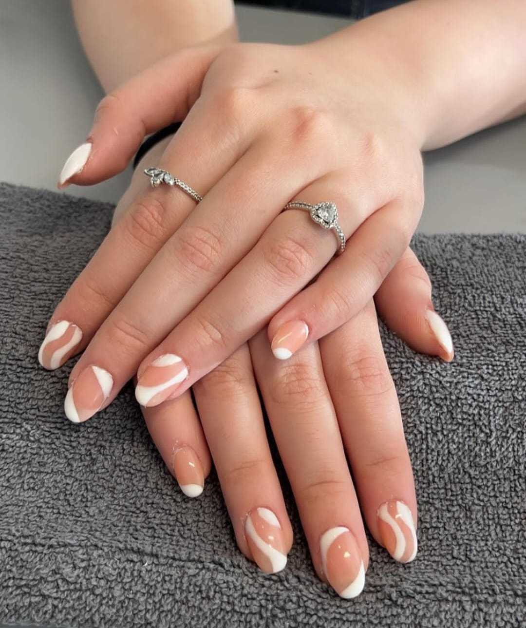 Elegant hands with heart-shaped ring and white swirl nail design on a grey towel.