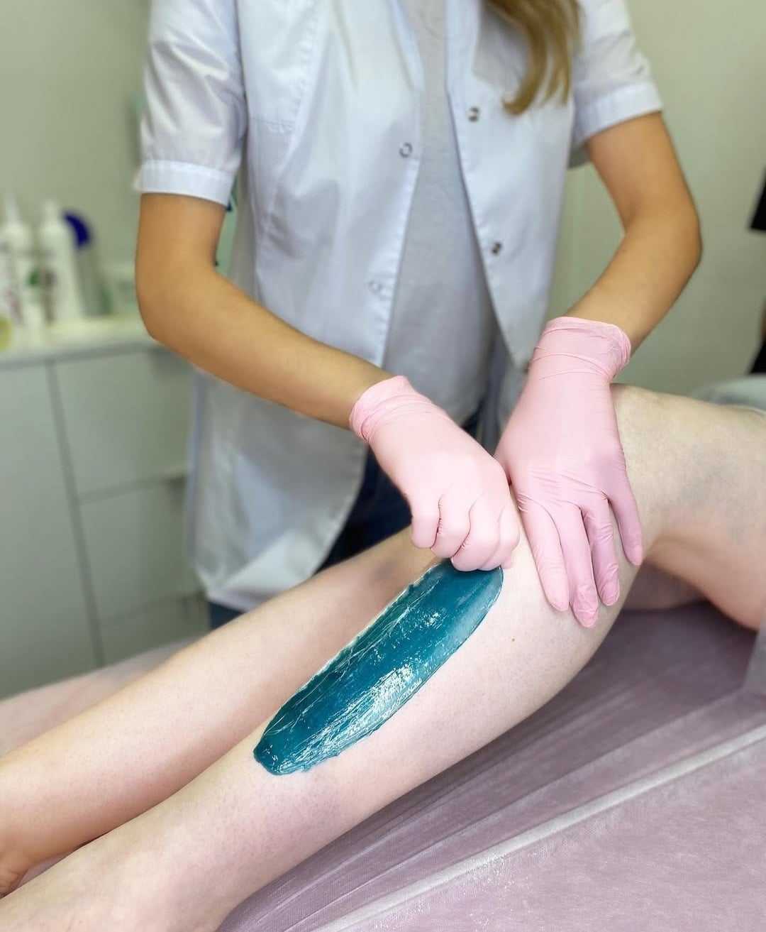 Esthetician applying wax on client's leg in a spa setting.